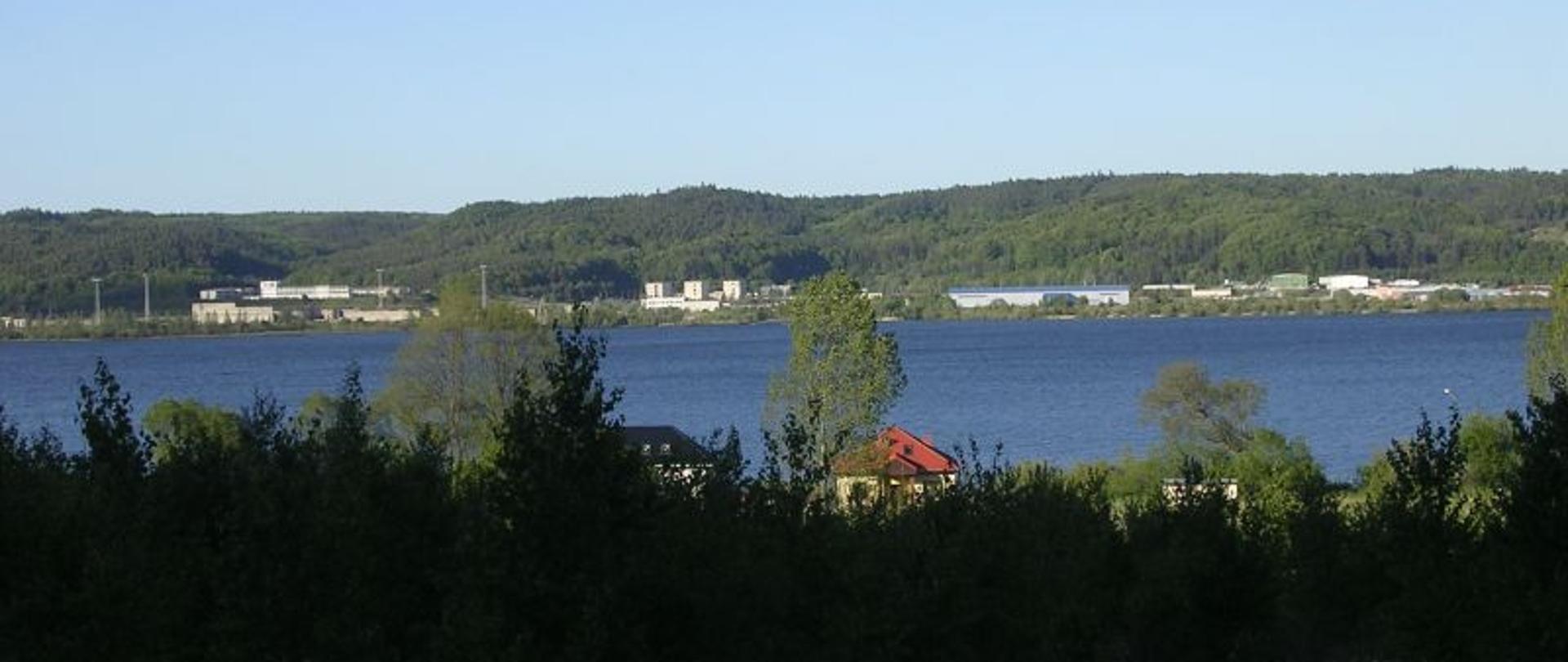 Zdjęcie pokazujące pozostałości po elektrowni jądrowej w Żarnowcu panorama nad jeziorem w tle widoczne pozostałości po zabudowaniach elektrowni jądrowej.