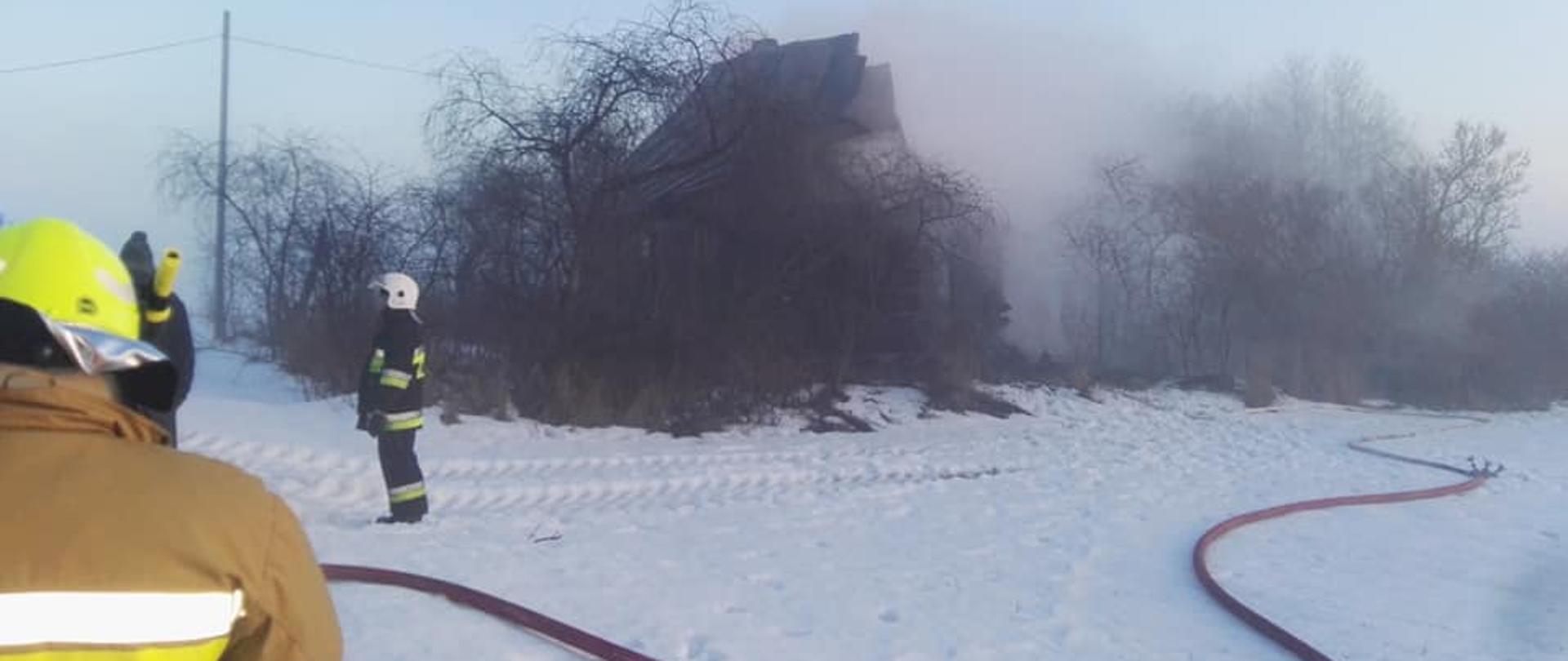 Na zdjęciu widać budynek pustostanu, który uległ spaleniu oraz strażaków podczas akcji gaśniczej. 