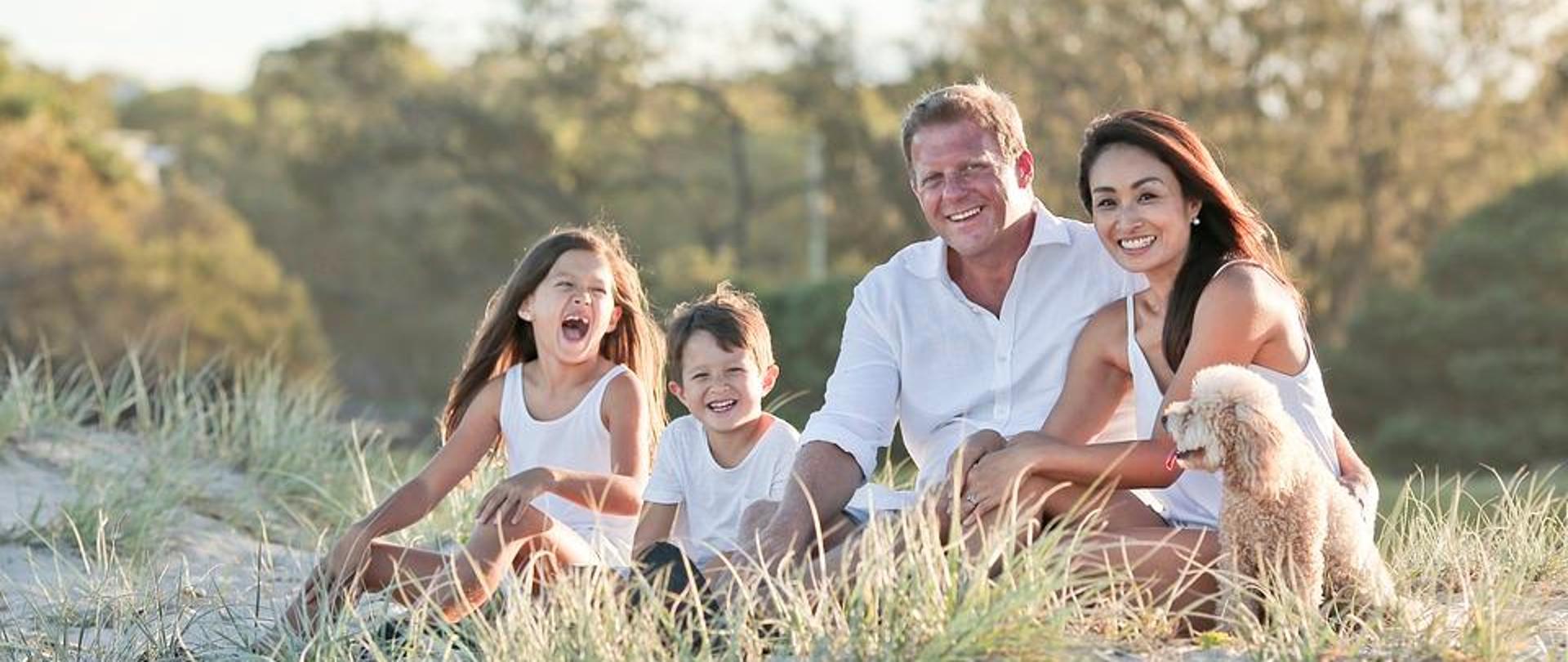 uśmiechnięci rodzice z dwójką dzieci siedzą na łące 