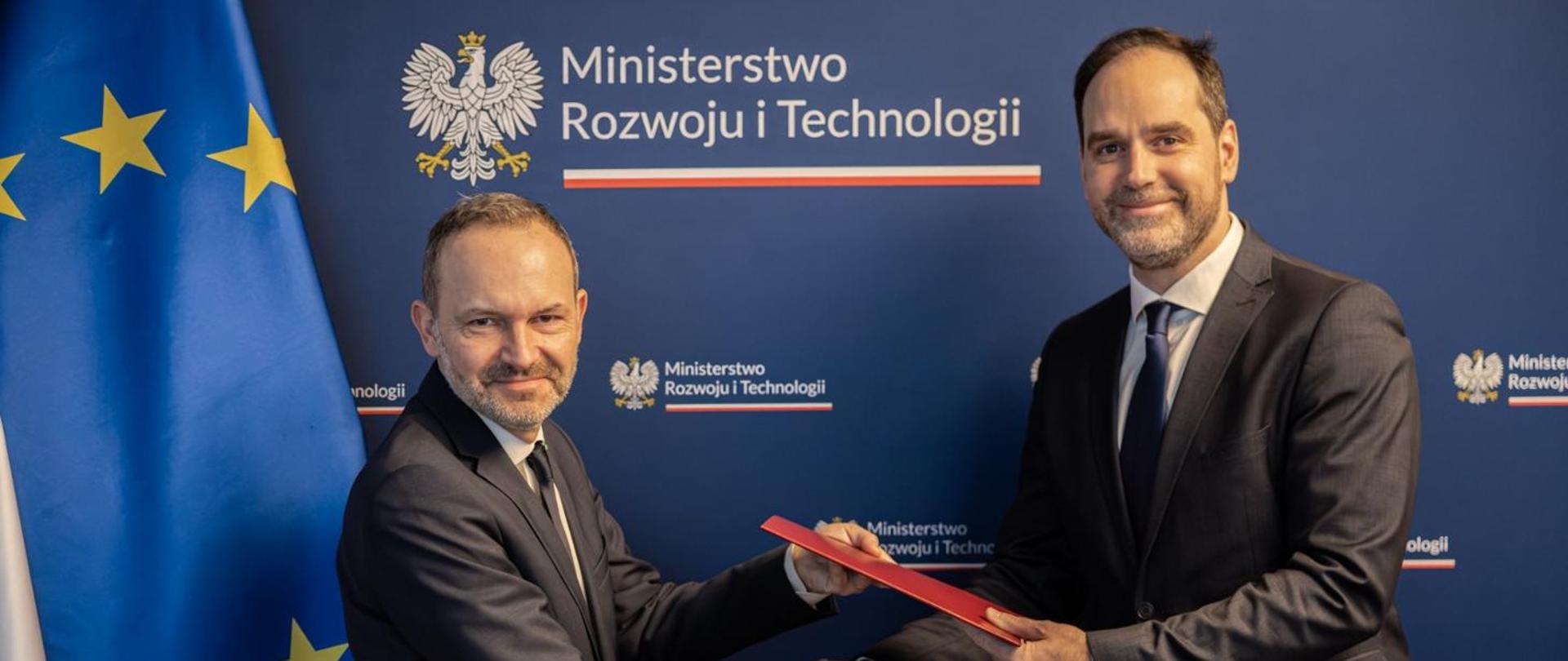 Na zdjęciu widać ministra Krzysztofa Hetmana i wiceministra Ignacego Niemczyckiego. W tle baner MRiT, a po prawej stronie flagi Polski i UE.
