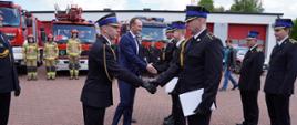 Na zdjęciu komendant powiatowy PSP w Łowiczu wraz z wicestarostą powiatu łowickiego gratulują funkcjonariuszom KP PSP w Łowiczu. W tle strażacy JRG i KP PSP w Łowicz, a za nimi samochody bojowe i operacyjne tutejszej Komendy.