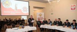 Sala obrad. Na pierwszym planie - w środku i z prawej strony - prezydium zebrania. W głębi po lewej stronie członkowie orkiestry OSP.