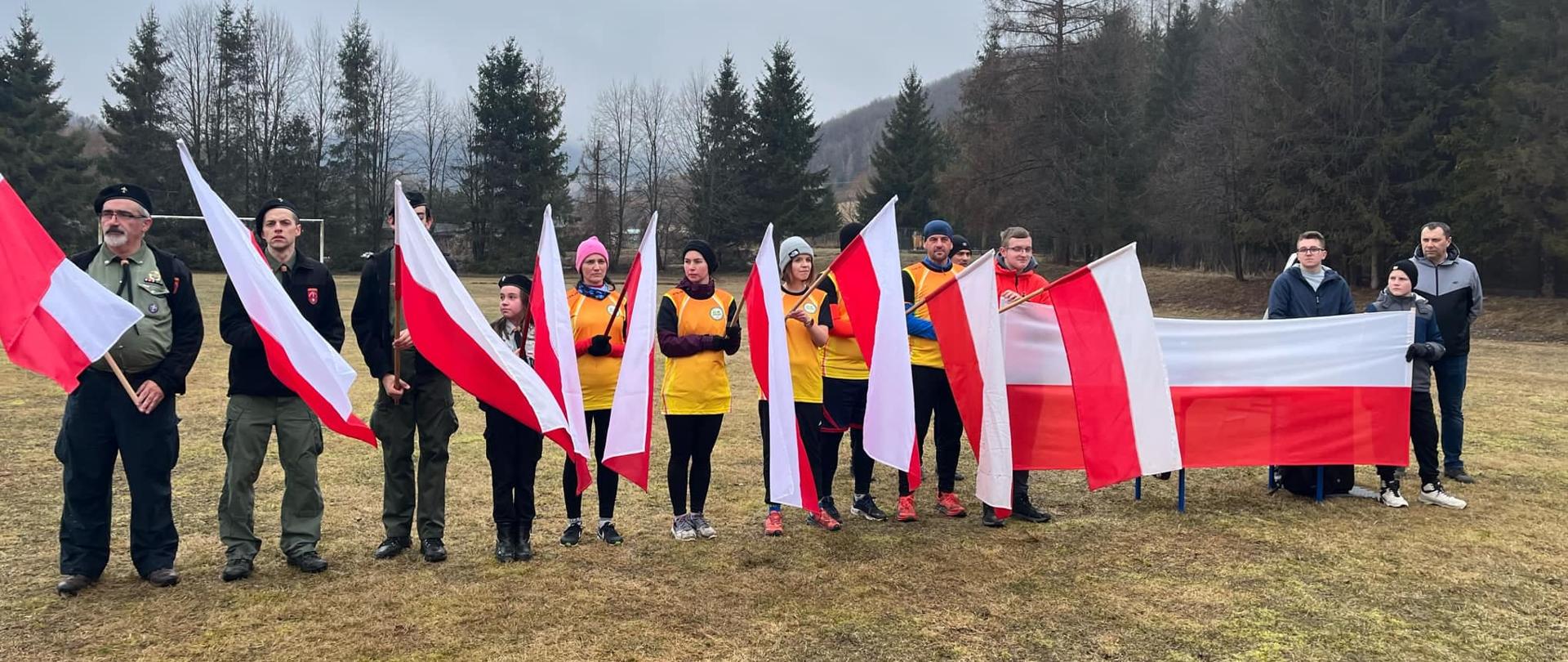 Uczestnicy z biało-czerwonymi flagami ustawieni w szeregu na boisku.