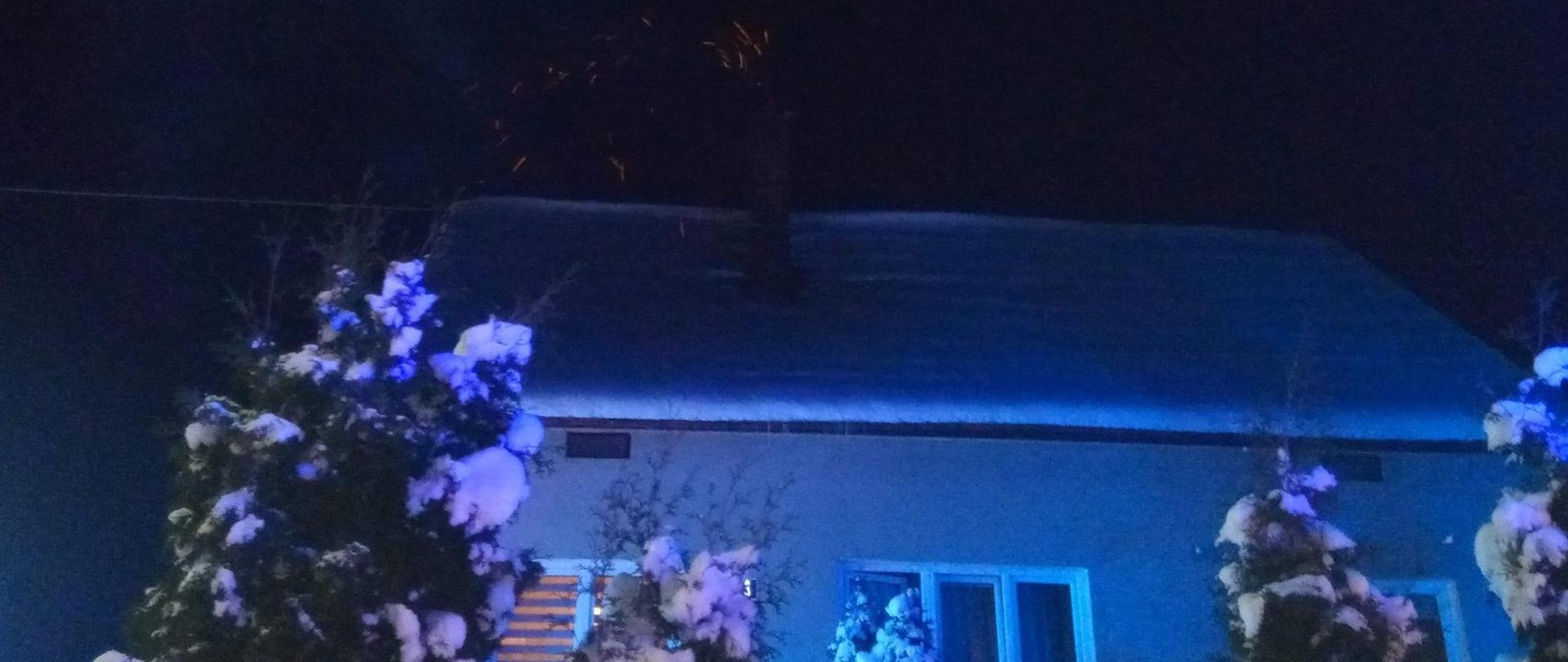 Ośnieżony budynek mieszkalny. Z komina wydobywają się iskry.