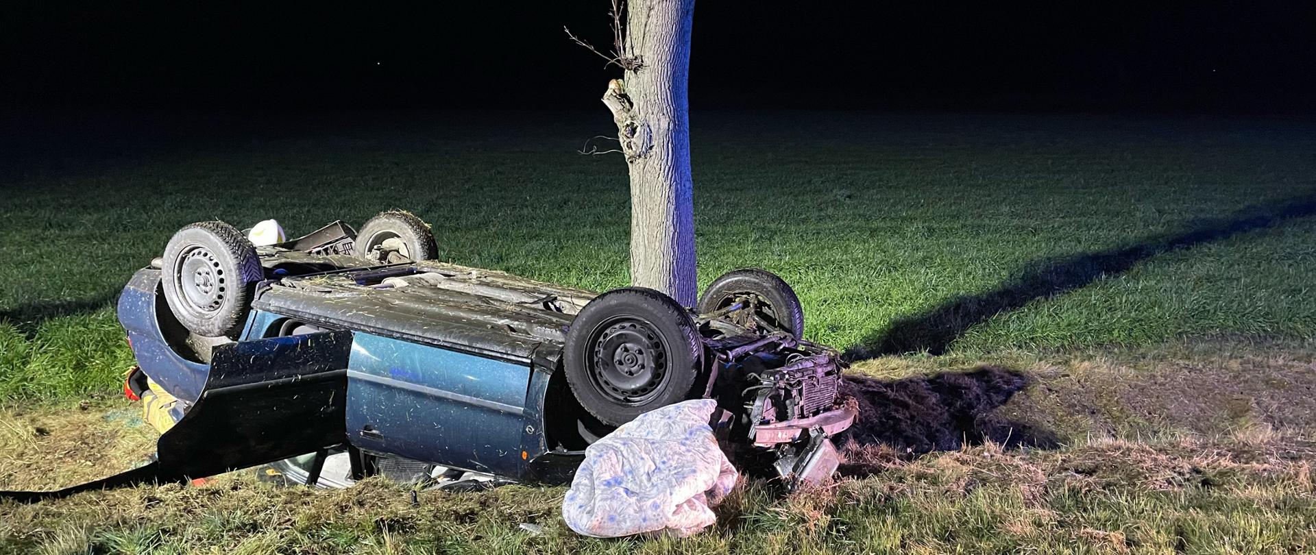 Zdjęcie w nocy. Wykonane z drogi publicznej. Widać pobocze, oraz rozbity pojazd. Oświetlenie sztuczne.