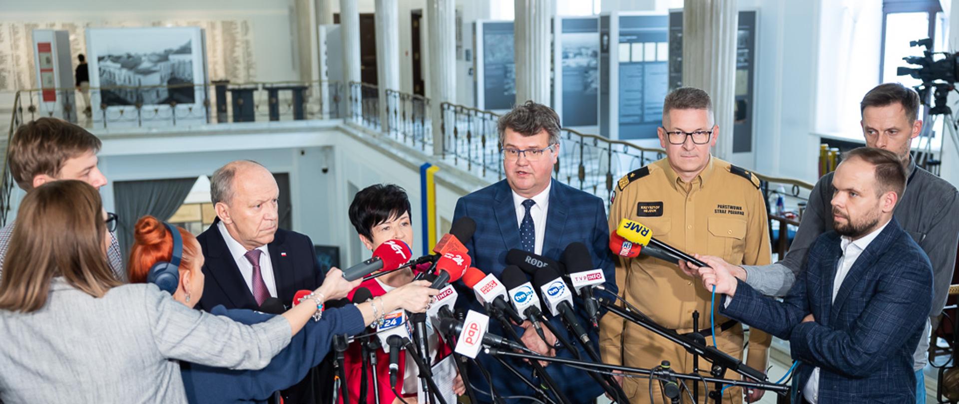 Zdjęcie przedstawia Wiceministra MSWiA Macieja Wąsika, przewodniczącego Parlamentarnego Zespołu Strażaków Zbigniewa Chmielowca, poseł Joannę Borowiak oraz zastępcę komendanta głównego PSP nadbryg. Krzysztofa Hejduka podczas briefingu prasowego dotyczącego dotacji dla Młodzieżowych Drużyn Pożarniczych.