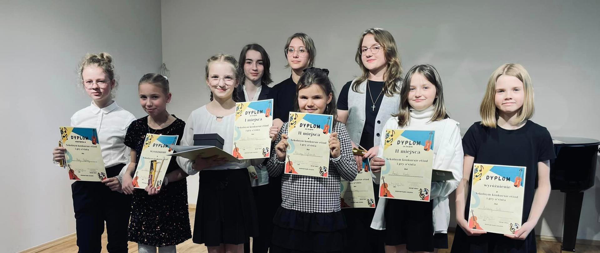 Grupa uczniów stoi na scenie sali koncertowej, w rękach trzymają dyplomy za udział w konkursie