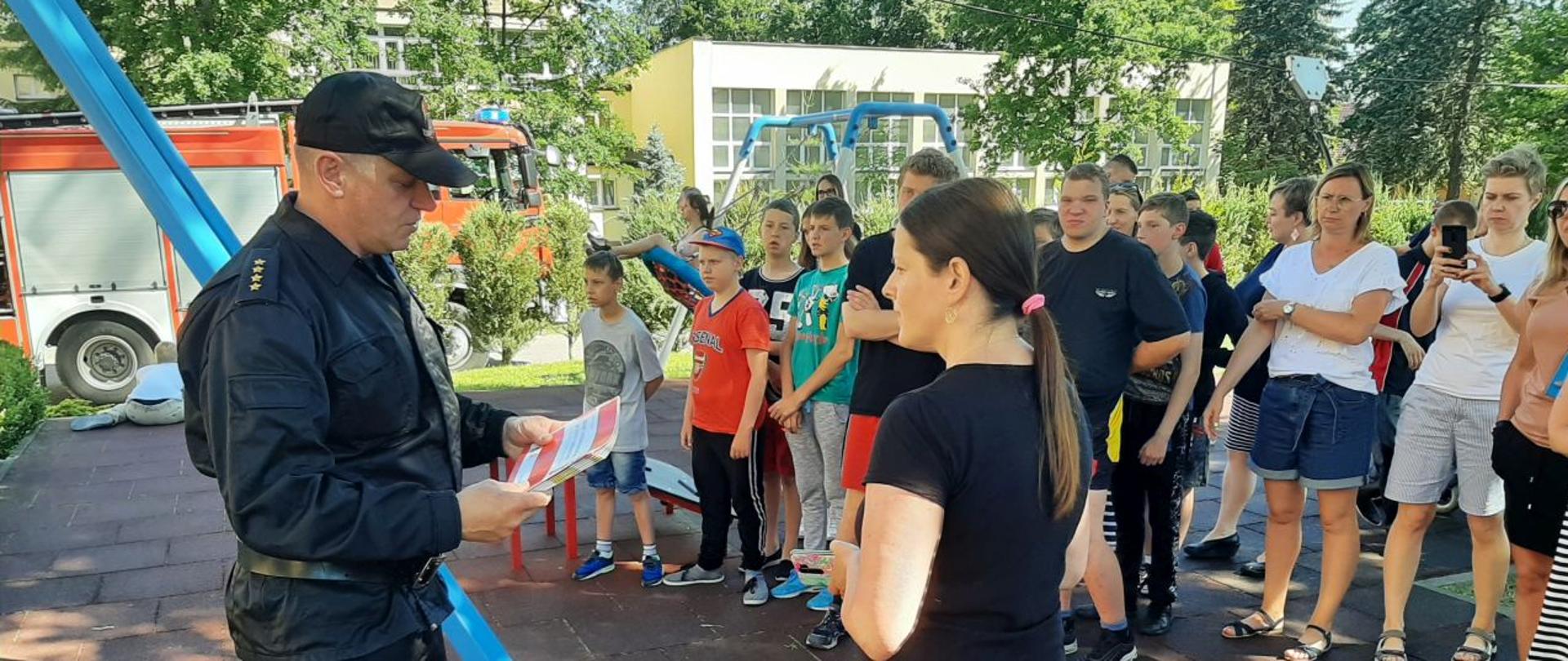 Widoczny strażak PSP wręczający książeczki edukacyjne wychowankom