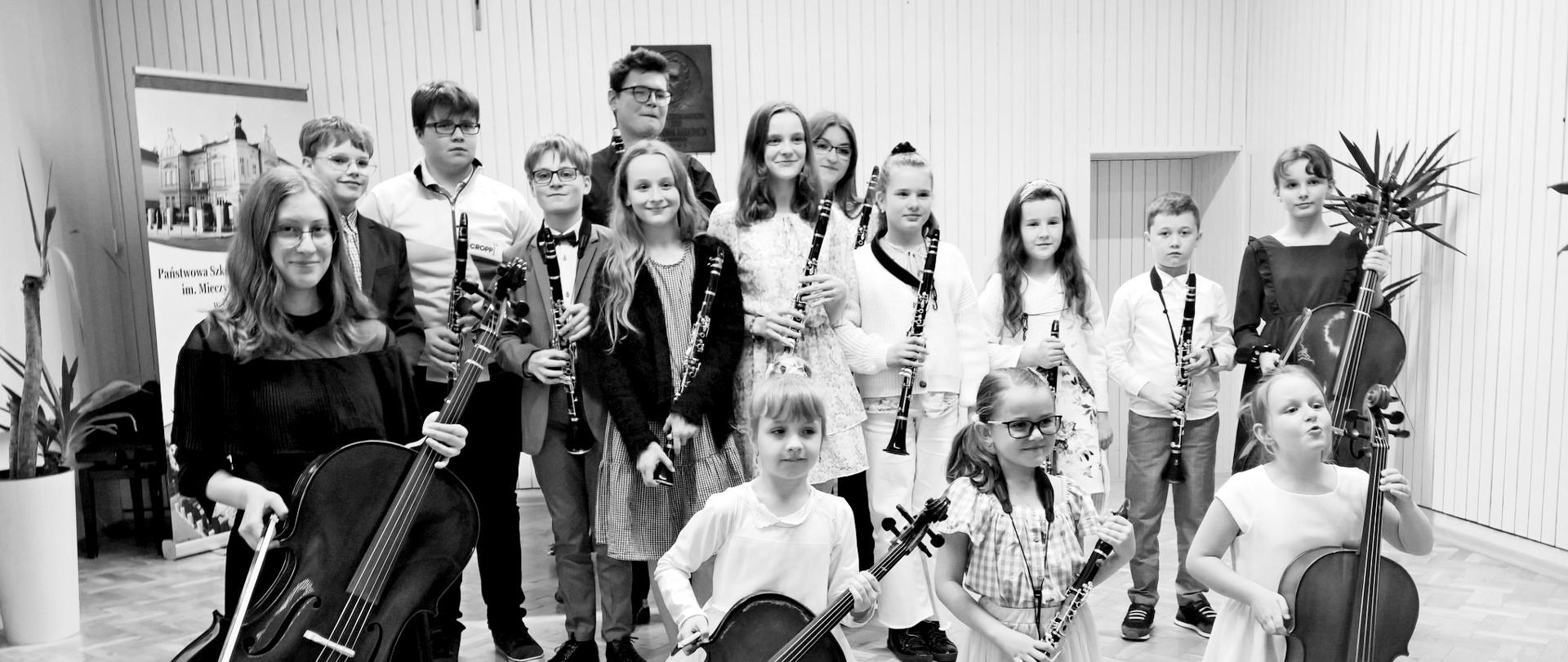 Zdjęcie uczniów na scenie trzymających klarnety i wiolonczele po koncercie zatytułowanym - Wiosenne Inspiracje