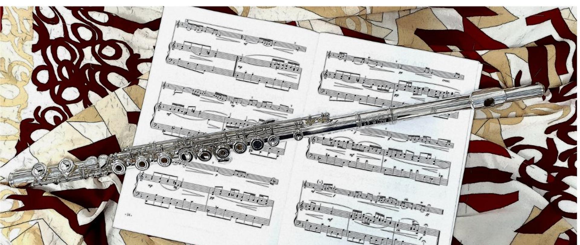 Na zdjęciu widnieje kolorowy materiał w szlaczki, na którym ułożone są otwarte nuty a na nich flet.
