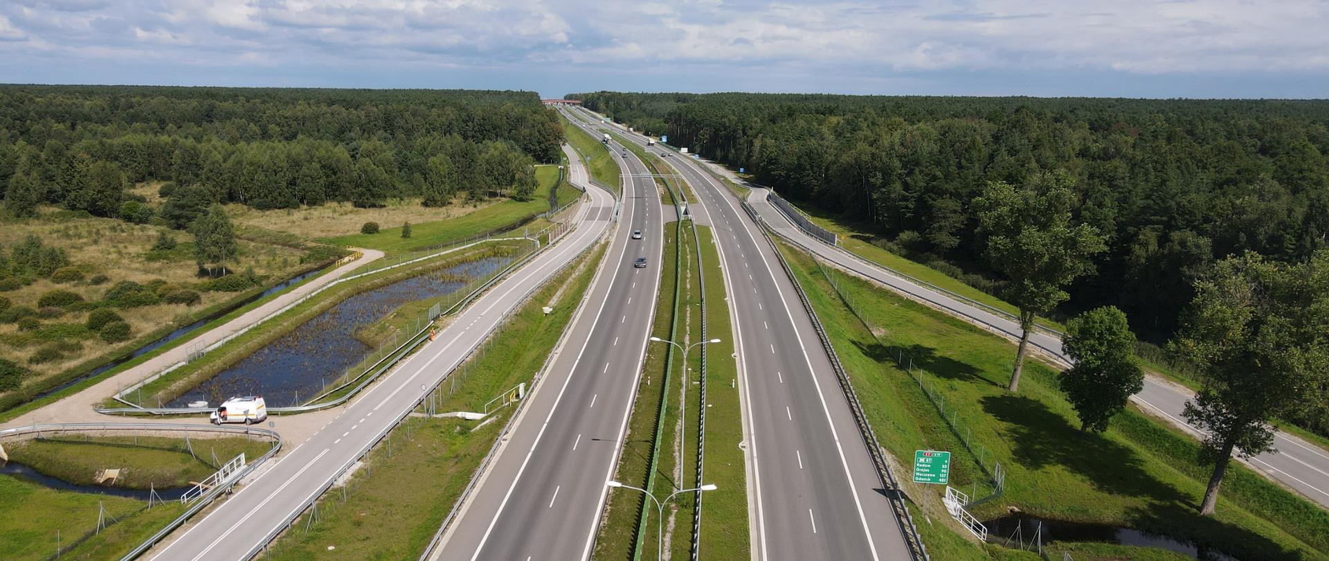 S7 przy granicy województwa świętokrzyskiego i mazowieckiego - dwujezdniowa droga ekspresowa z równoległymi drogami po obu stronach. Po lewej zbiornik retencyjny i ciek wodny. W oddali przejście dla zwierząt pod drogą, a dalej nad drogą. 