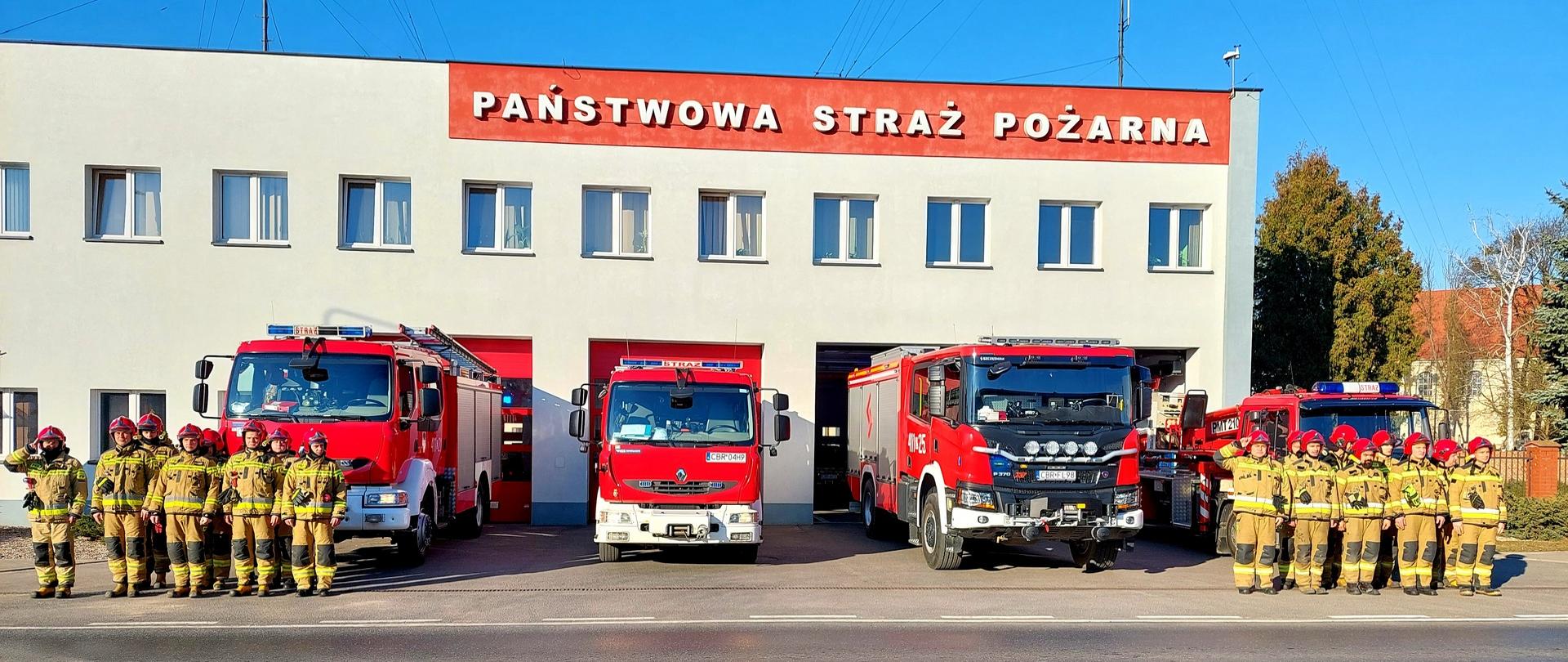 Zdjęcie przedstawia strażaków z Brodnicy oddających cześć pamięci strażaków z Ukrainy poległych podczas działań. Strażacy przed samochodami Komendy w Brodnicy. W tle budynek Komendy.