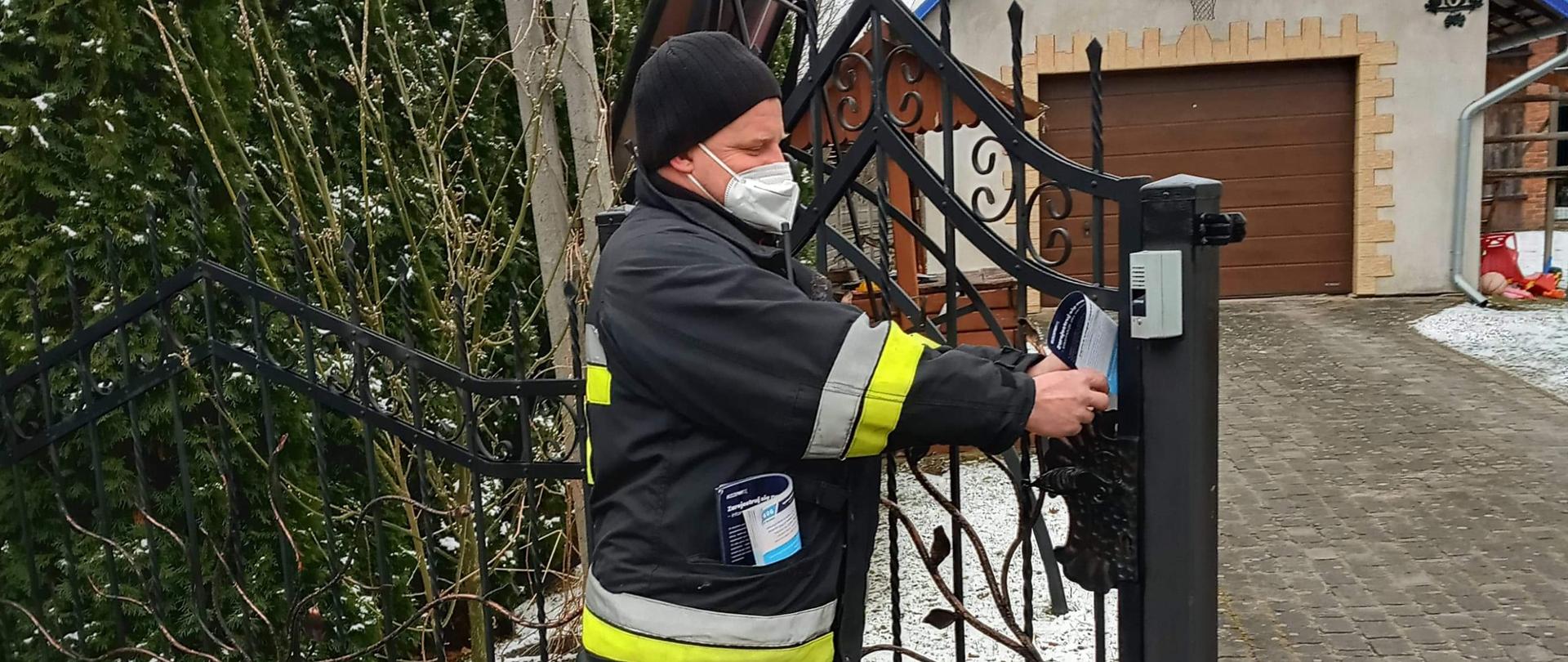 Na zdjęciu widzimy strażako OSP, który wkłada ulotkę do skrzynki na listy.