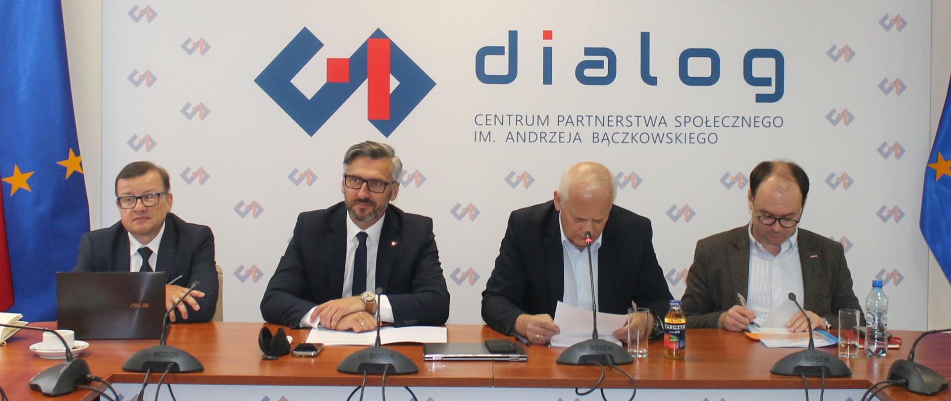 Na zdjęciu widnieje stół prezydialny za którym siedzą: Pan Mirosław Motyka - Prezes Hutniczej Izby Przemysłowo- Handlowej, Pan Waldemar Sługocki – Sekretarz Stanu w Ministerstwie Rozwoju i Technologii, Pan Andrzej Karol – Współprzewodniczący Zespołu ze strony związków zawodowych oraz Pan Sebastian Gajewski – Podsekretarz Stanu w Ministerstwie Rodziny, Pracy i Polityki Społecznej. W tle widnieje baner z napisem Centrum Partnerstwa Społecznego „Dialog” im. Andrzeja Bączkowskiego.