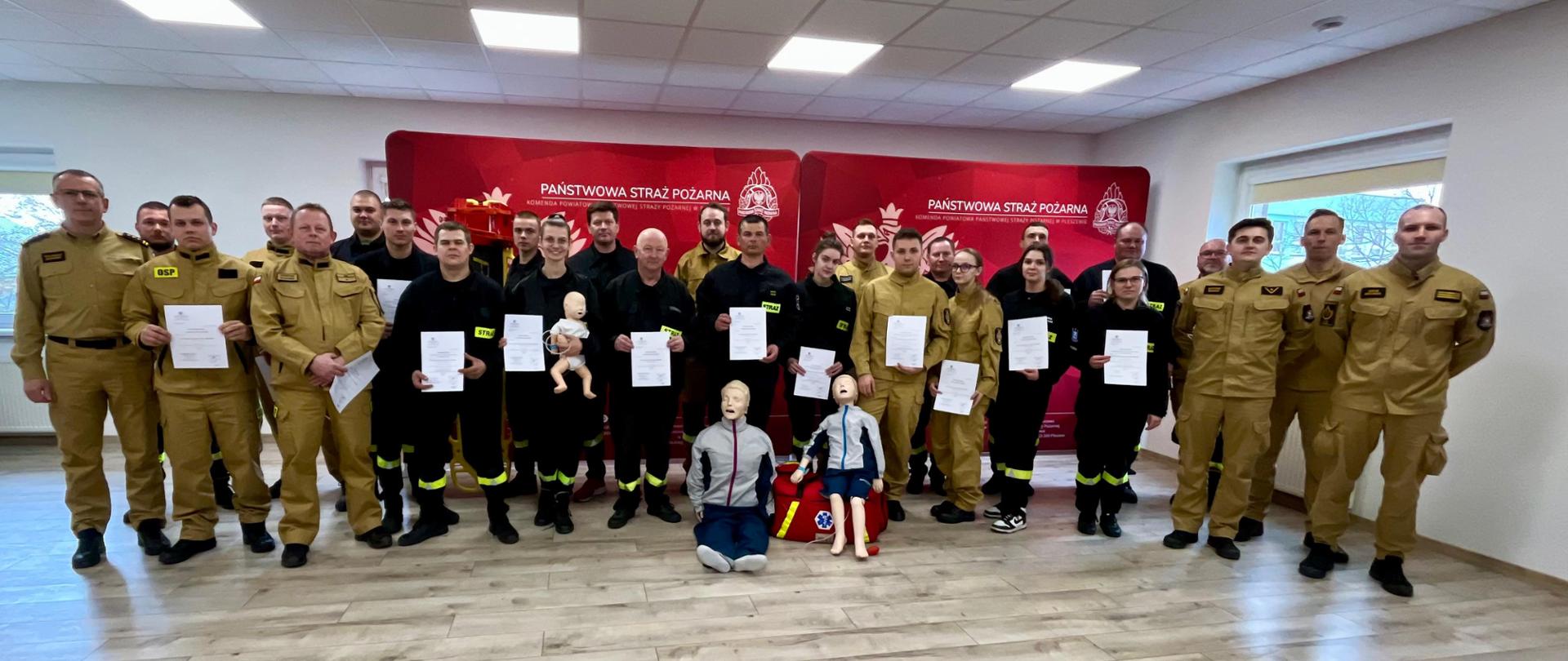 grupa osób w mundurach strażackich na sali wykładowej stojący z dyplomami po ukończonym kursie