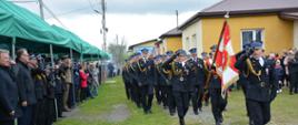 Defilada pododdziałów przed trybuną honorową. Na pierwszym planie salutujący strażak dowódca pododdziału.