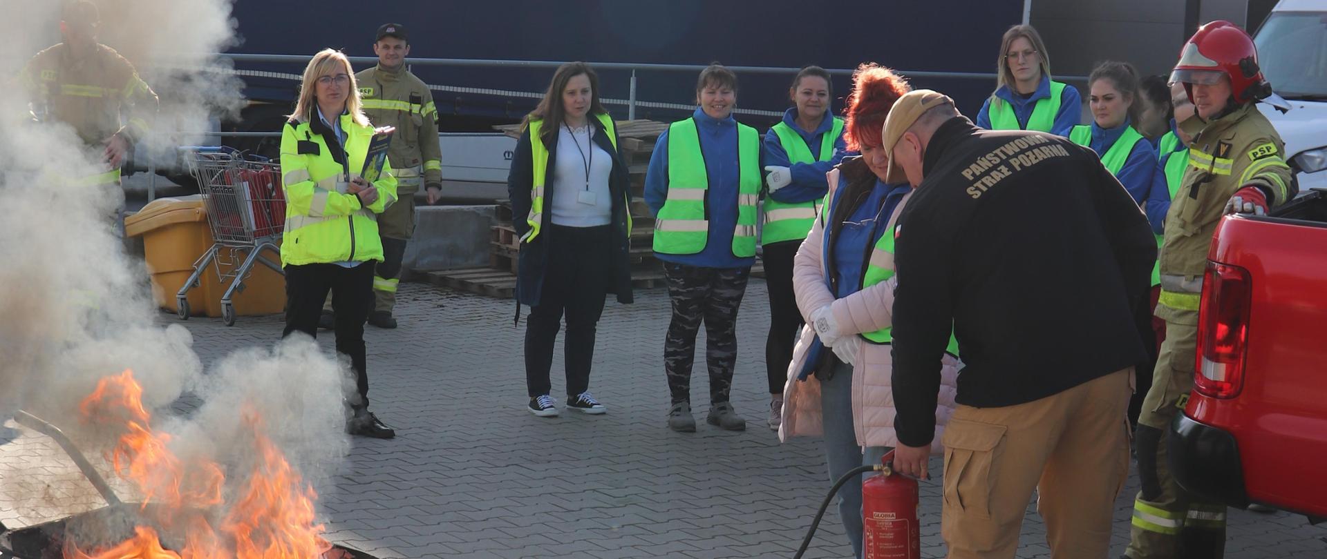 Osoby cywilne obserują strażaka gaszącego ogień.