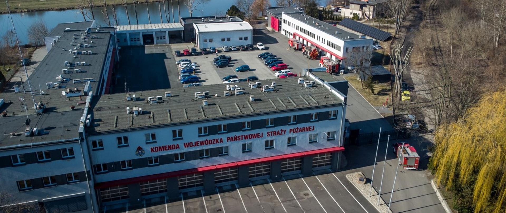 Samochody pożarnicze stojące na placu KW PSP Opole w trakcie przygotowania do przekazania. Zdjęcie wykonane z lotu ptaka. Na zdjęciu widoczny budynek KW PSP Opole.