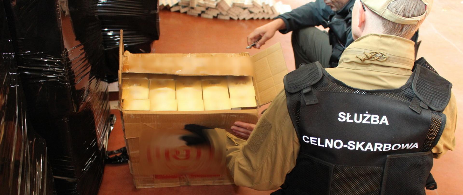 Funkcjonariusze Służby Celno-Skarbowej przed kartonem, w którym znajdują się nielegalne papierosy