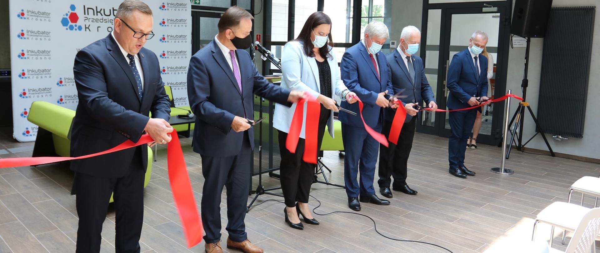 W pomieszczeniu 6 osób przecina wstęgę. Trzecia od lewej wiceminister Małgorzata Jarosińska-Jedynak.