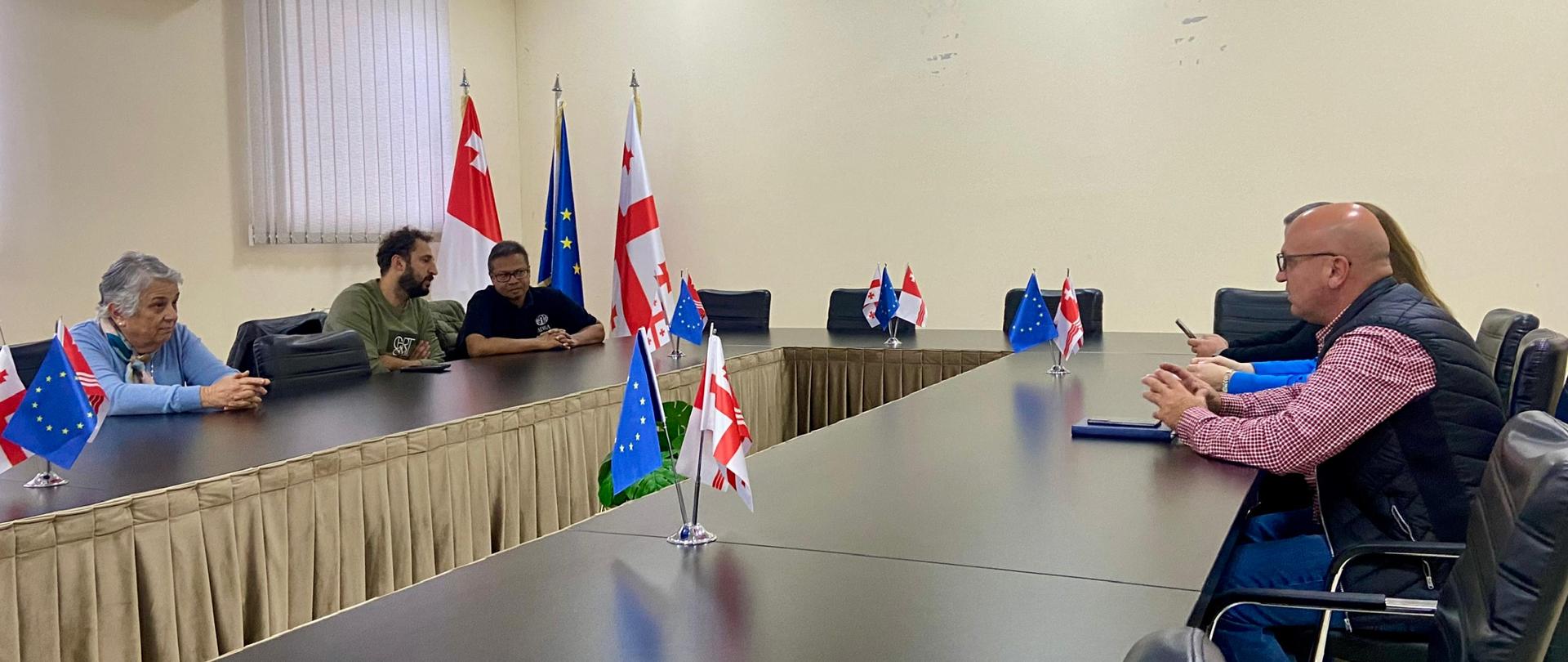 Przy stole z flagami Unii Europejskiej i Gruzji siedzą ludzie 