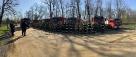 Na zdjęciu grupa strażaków podczas zbiórki. W tle stoją samochody gaśnicze.