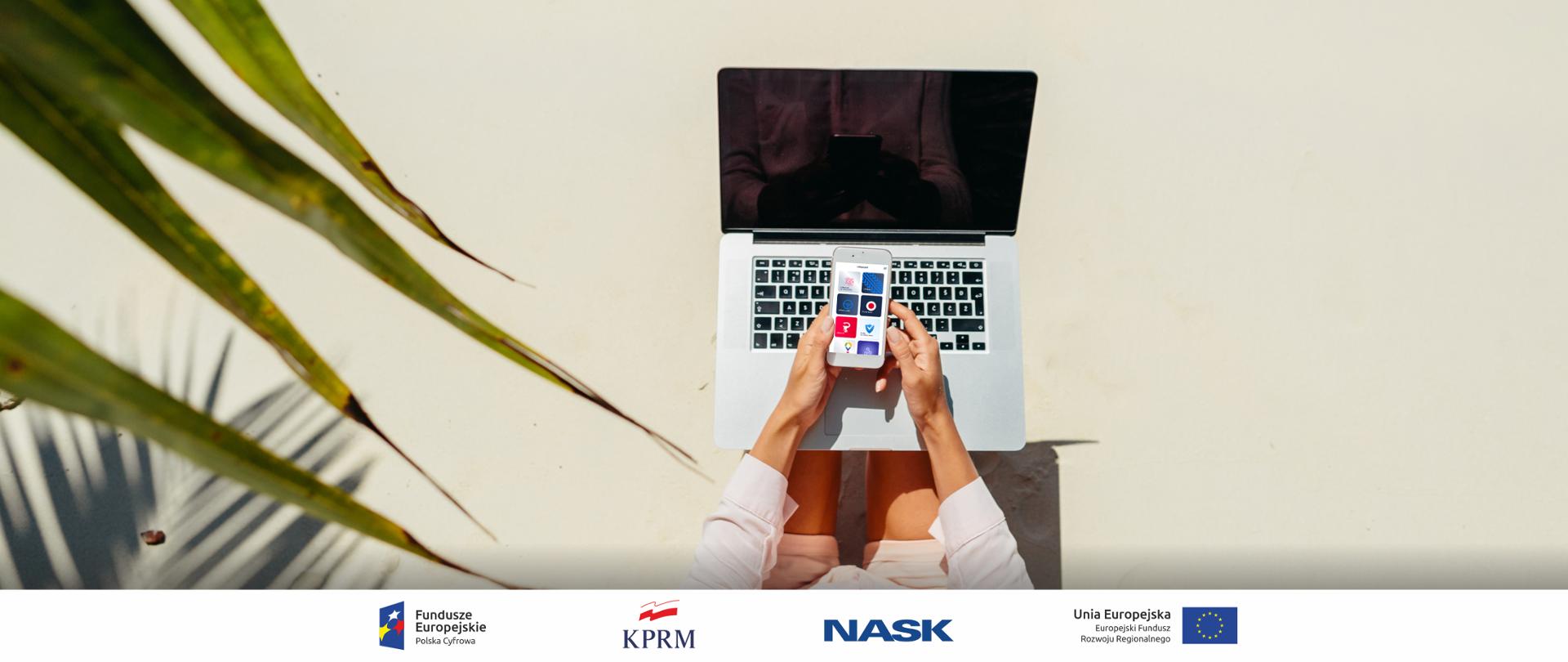 Zdjęcie z góry przedstawiające dziewczynę z laptopem na kolanach i smartfonem w rękach. Z lewej strony liście. 