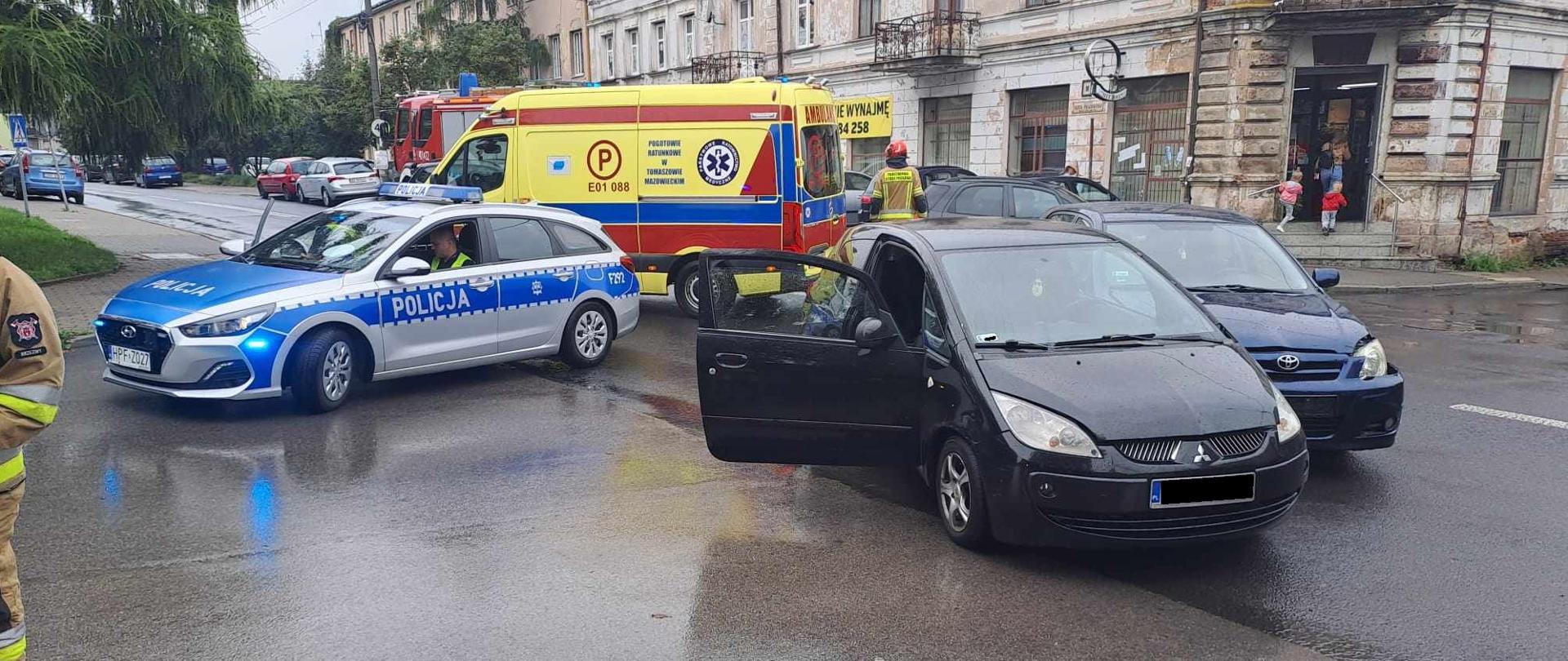 Skrzyżowania w centrum Brzeziny dwa samochody po kolizji granatowa Toyota oraz czarne Mitsubishi. Na drugim planie samochód Policji oraz ambulans.