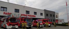 Na zdjęciu strażacy na tle samochodów pożarniczych i remizy