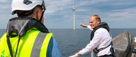 Premier Donald Tusk podczas wizyty na farmie wiatrowej Baltic Power. W tle turbina wiatrowa.