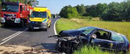 Uszkodzony pojazd poza jezdnią, ambulans wraz z pojazdem pożarniczym stoją na drodze 