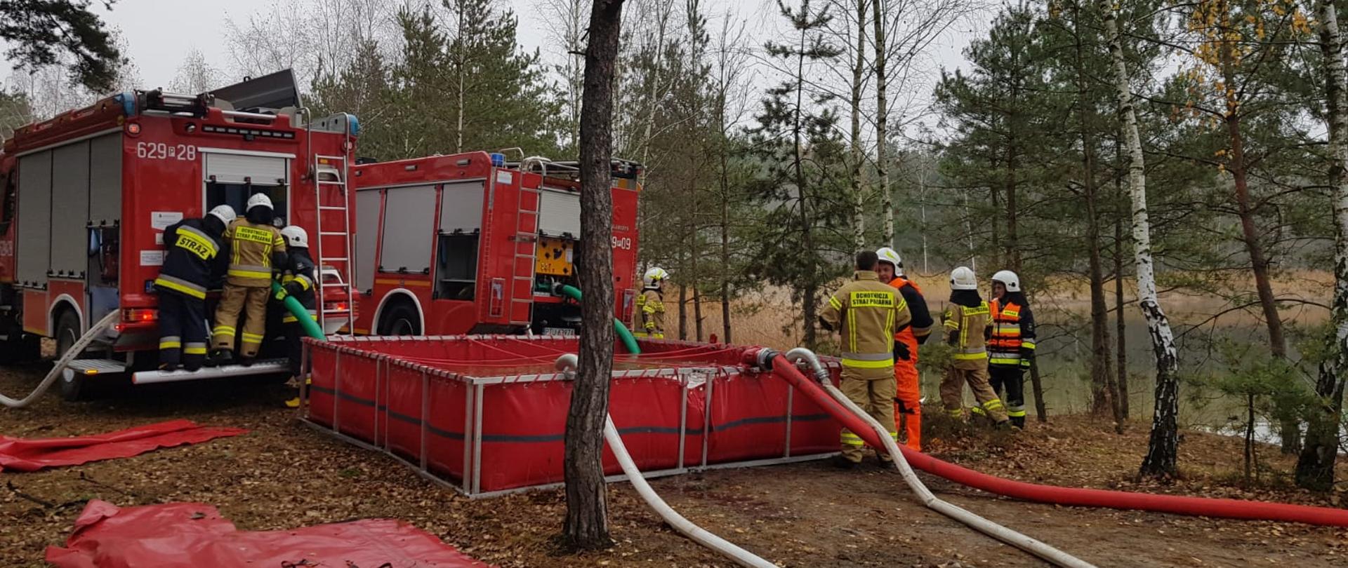 Strażacy w trakcie przepompowywania wody ze zbiornika przy użyciu pojazdów pożarniczych.