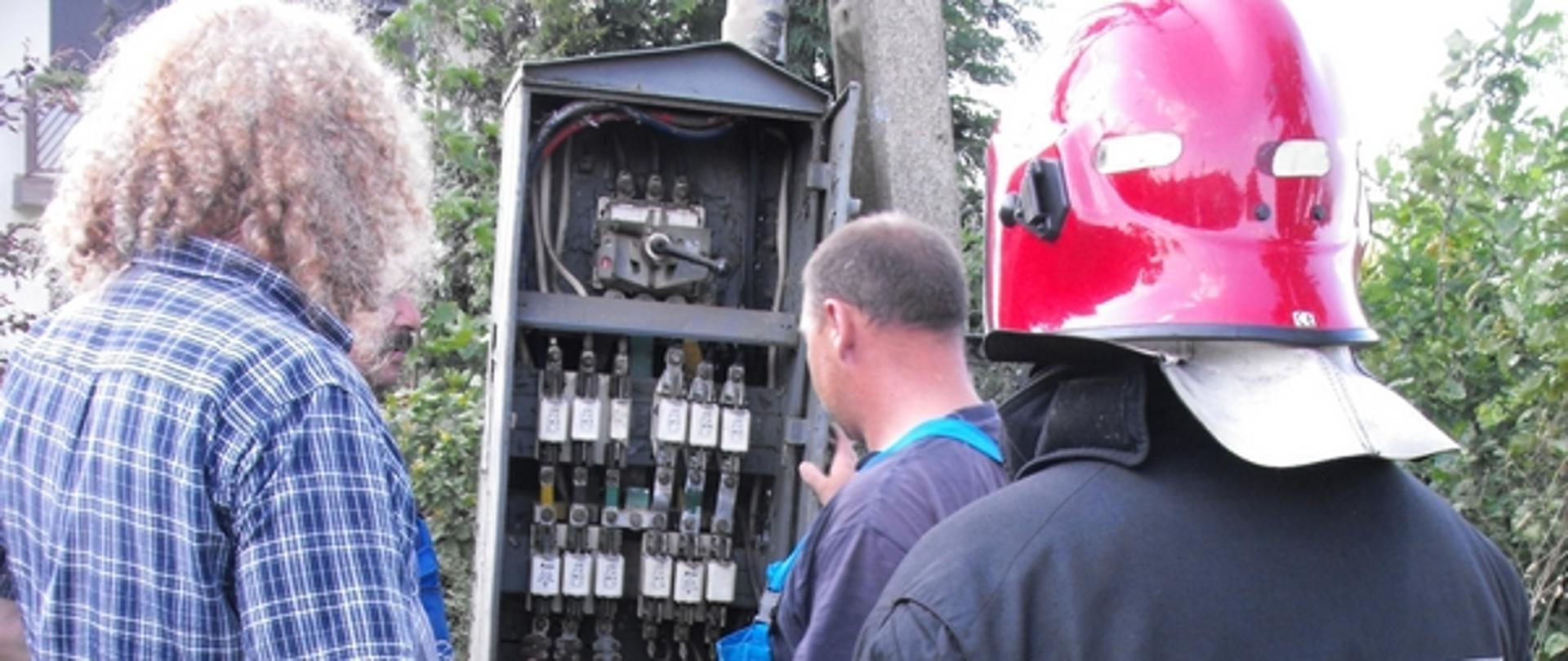 Zdjęcie pracowników zakładu energetycznego i strażaka przed tranformatorem