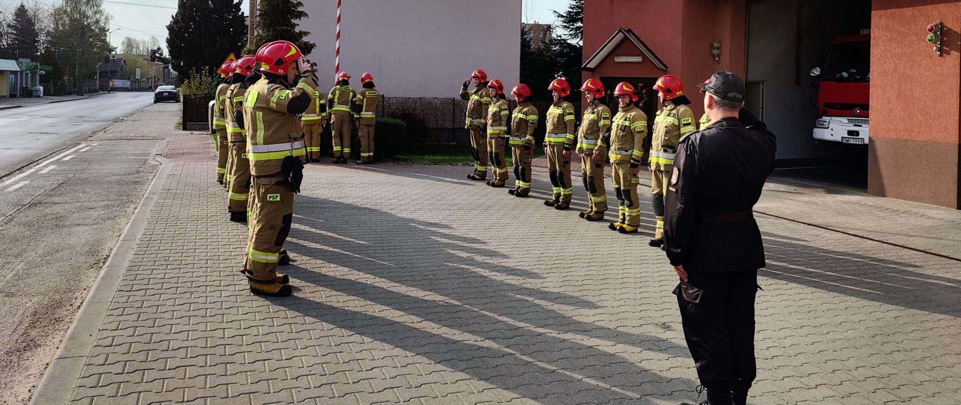 Zdjęcie przedstawia strażaków ustawionych w szyku podczas uroczystego wciągania flagi RP na maszt. 