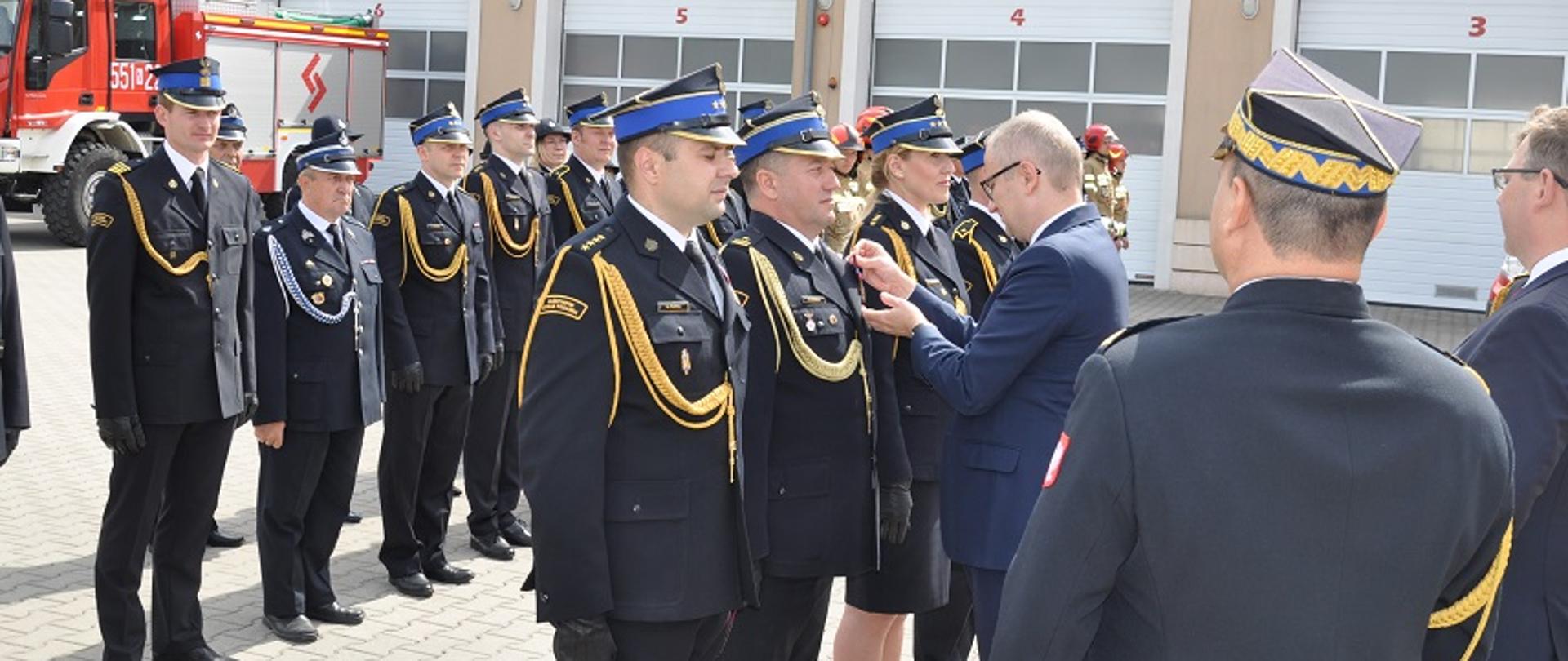 Mężczyzna w granatowym garniturze wręcza odznaczenia strażakom