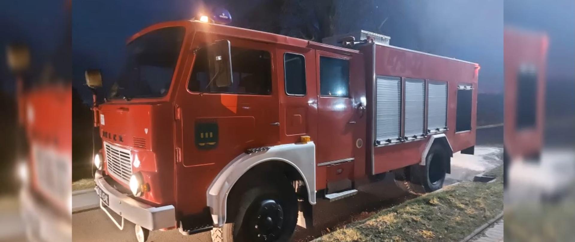 Zdjęcie przedstawia czerwony samochód ratowniczo-gaśniczy marki JELCZ. Samochód sfotografowany podczas działań w porze nocnej.