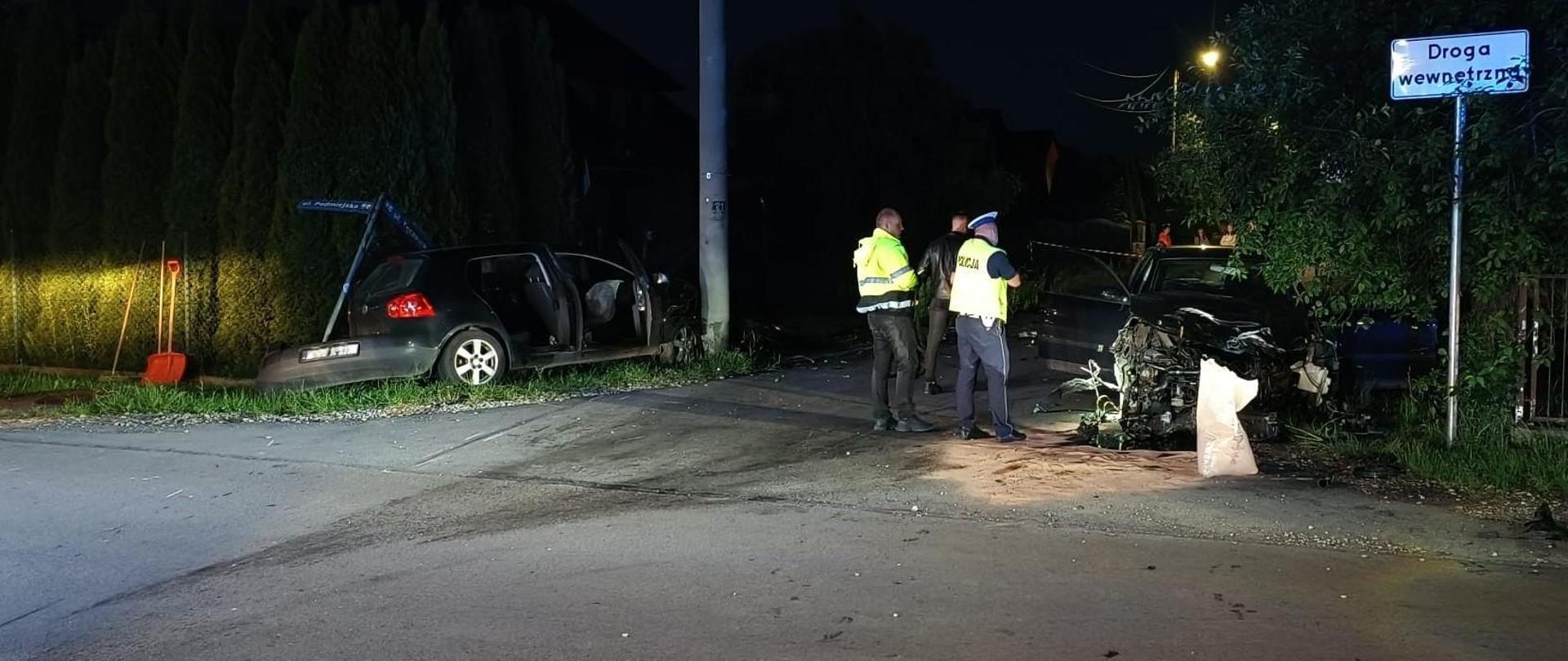 Zdjęcie przedstawia skrzyżowanie gdzie doszło do wypadku. Po lewej stronie jeden ze zniszczonych samochodów stoi na poboczu. Przy drugim znajdującym się po prawej stronie stoi dwóch funkcjonariuszy Policji.