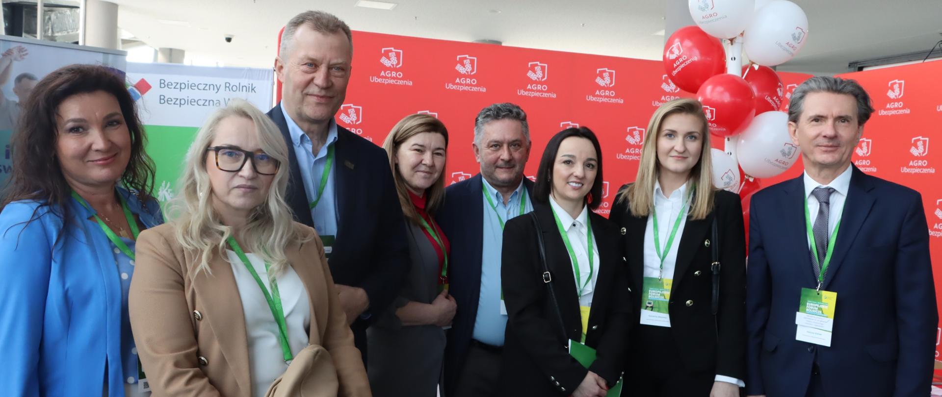 Pięć kobiet i trzech mężczyzn pozują do zdjęcia lekko się uśmiechając na tle rollupów KRUS i ścianki Agro Ubezpieczeń.