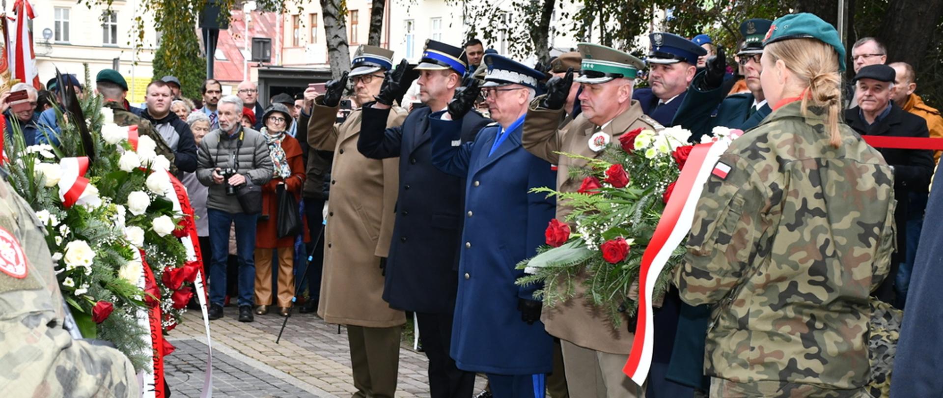 Zdjęcie zrobione na zewnątrz podczas uroczystych obchodów Narodowego Święta Niepodległości w Rzeszowie. Delegacja przedstawicieli służb mundurowych składa kwiaty pod pomnikiem Marszałka Piłsudskiego. Oficerowie stoją na baczność i salutują. Delegacji znajdują się oficerowie Wojska Polskiego, Policji, Państwowej Straży Pożarnej, Straży Granicznej, Służby Więziennej