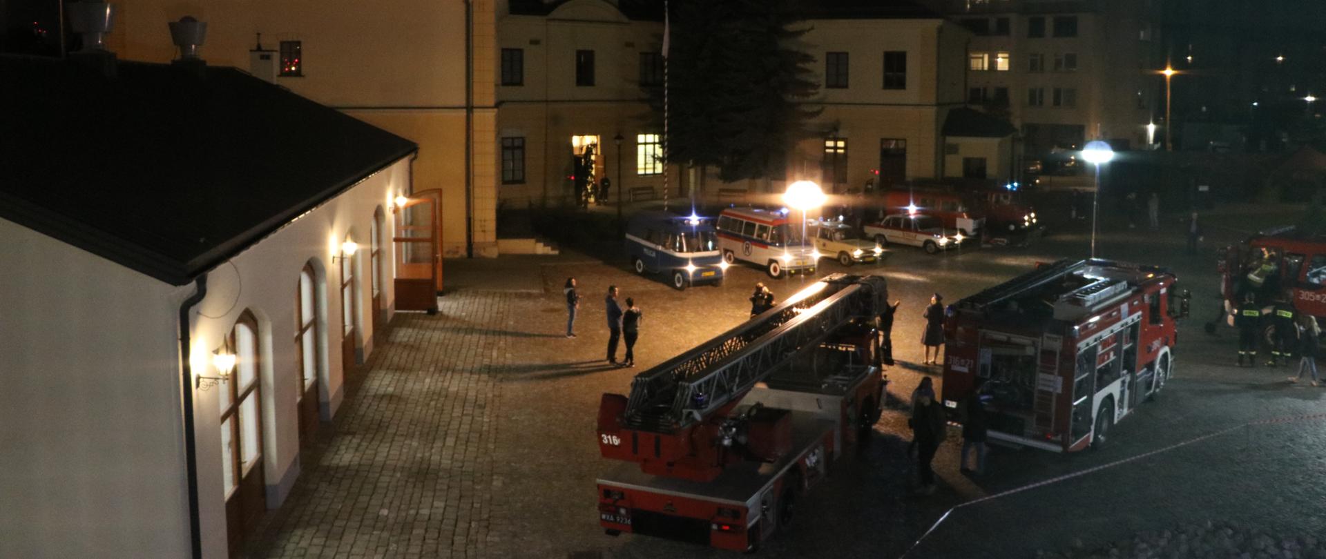 Plac wewnętrzny Jednostki Ratowniczo - Gaśniczej numer 5 Komendy Miejskiej Państwowej Straży Pożarnej miasta stołecznego Warszawy, na którym ustawione są współczesne pojazdy pożarnicze oraz odrestaurowane samochody użytkowane przez straże pożarne, Milicję Obywatelską oraz Pogotowie Ratunkowe w drugiej połowie ubiegłego wieku.