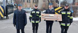 Odchodzący na zaopatrzenie emerytalne funkcjonariusz trzyma w rękach pamiątkową szablę ozdobną, towarzyszą mu Komendant Miejski Państwowej Straży Pożarnej w Zabrzu, dowódca jednostki ratowniczo-gaśniczej oraz zastępca dowódcy jednostki ratowniczo-gaśniczej.