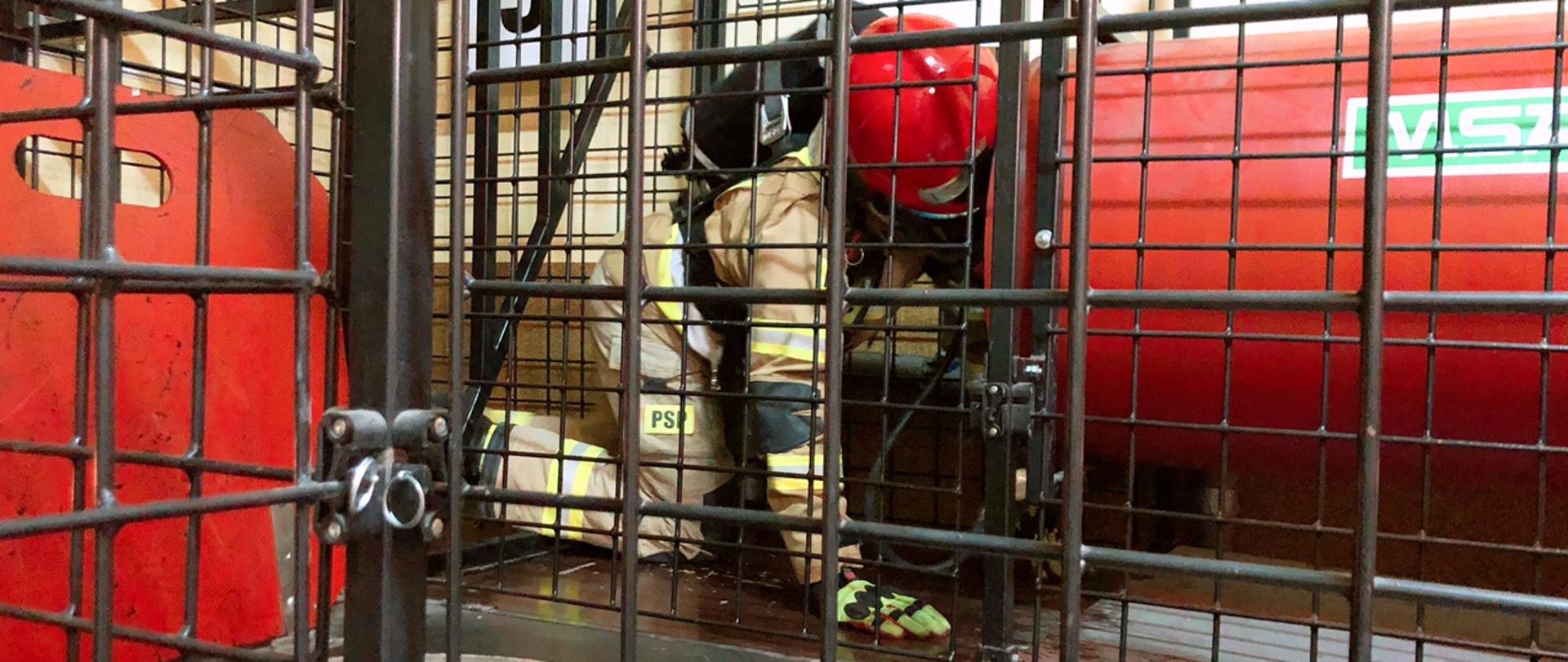 Na czwartym zdjęciu strażak w ubraniu specjalnym
z założoną na twarzy maską i aparatem powietrznym na plecach oraz w hełmie chroniącym jego głowę pokonuje przeszkody w komorze dymowej. Przeszkody wykonane są z metalowych elementów. Test odbywa się w całkowitym zaciemnieniu
i zadymieniu.
