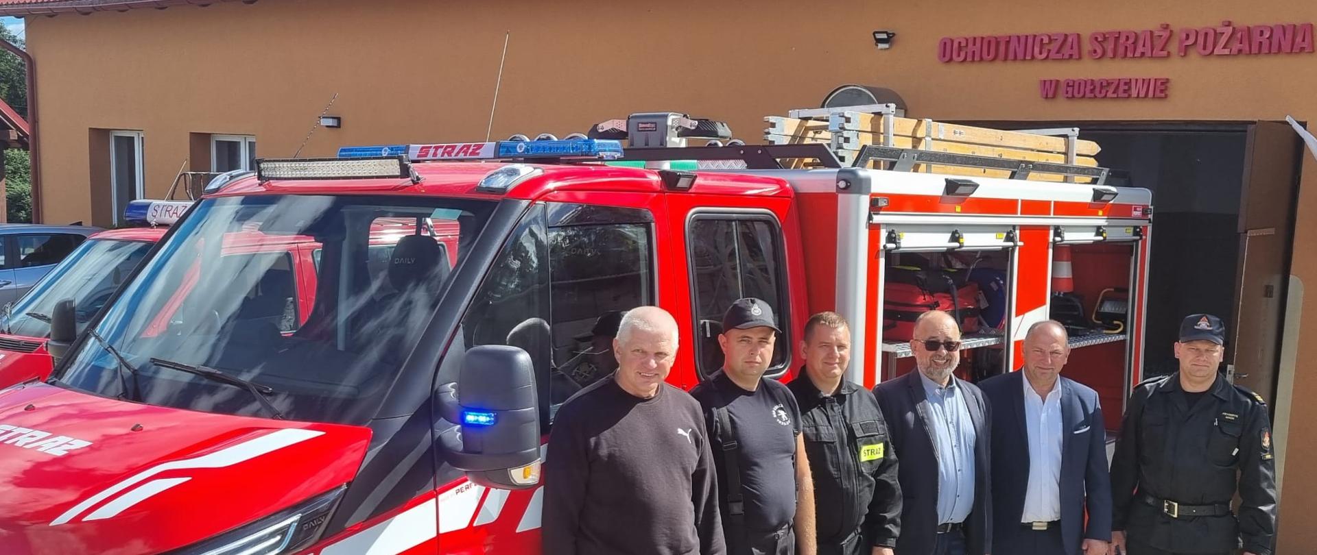 Przed remizą strażacką OSP w Gołczewie stoi nowy wóz strażacki. Wzdłuż jego dłuższego boku stoją w rzędzie goście wizytujący remizę (m.in. Zastępca Komendanta KP PSP w Bytowie, Prezes OSP, Prezes ZOSP i wójt gminy).