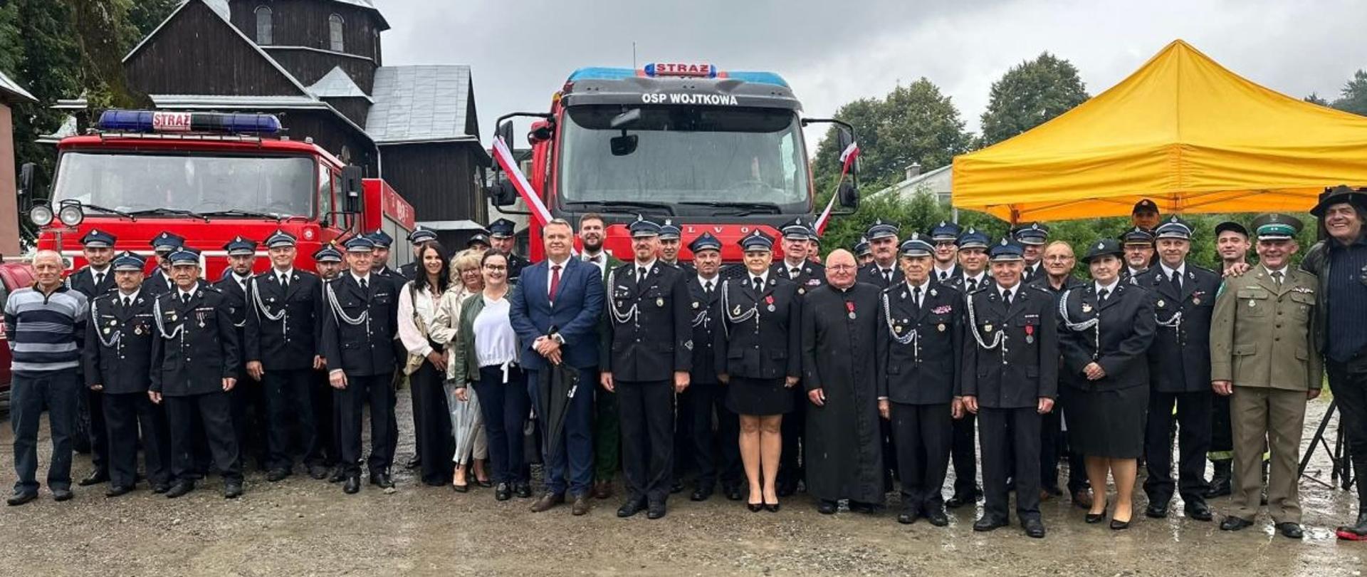 Na zdjęciu widać strażaków jednostki OSP w mundurach galowych, burmistrza Ustrzyk Dolnych oraz zaproszonych gości. Za wszystkimi zgromadzonymi stoją dwa samochody gaśnicze. W tym nowy wóz marki Volvo.