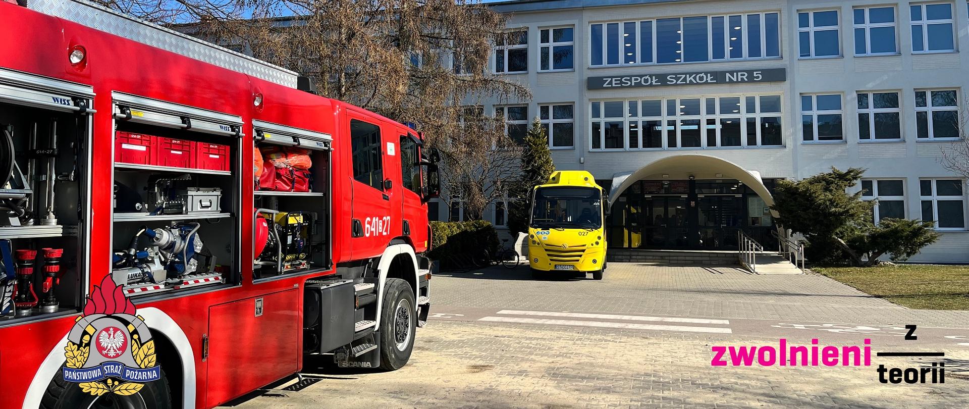 Po lewej stronie samochód straży pożarnej w otwartymi skrytkami na tle zespołu szkół nr 5 w Tychach, przed wejściem do szkoły zaparkowany jest autobus PKM Tychy 