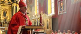 Ksiądz Biskup przy mównicy kościelnej. W tle kilkunastu księży kapelanów, z tle wnętrze prezbiterium.