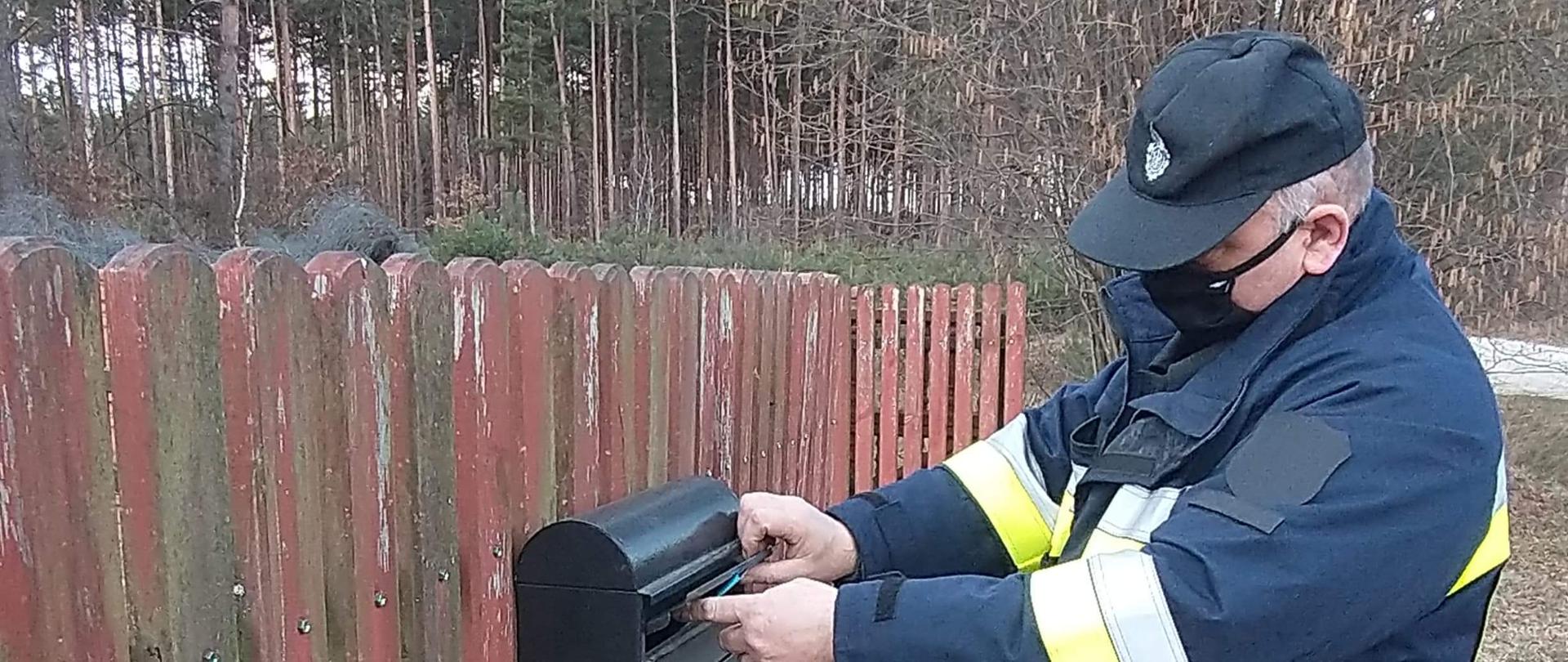 Na zdjęciu widzimy druha wrzucającego ulotkę do skrzynki na listy. W tle widać drzewa iglaste.