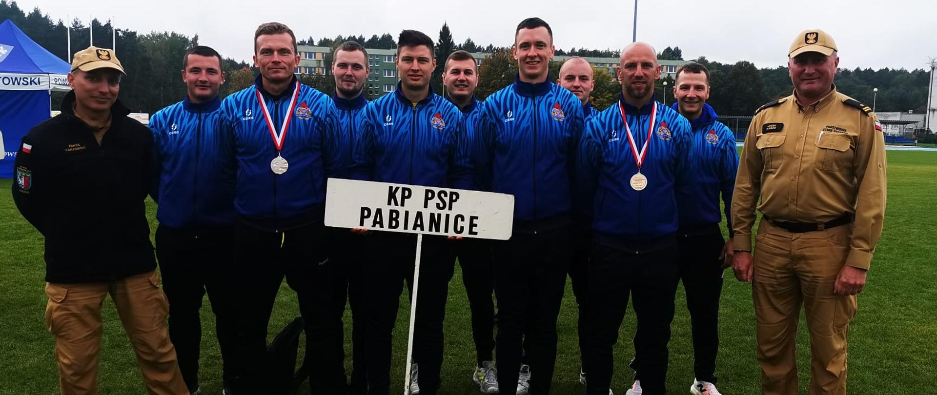 Zdjęcie reprezentacji Komendy Powiatowej PSP podczas XXIII Mistrzostw Województwa Łódzkiego Strażaków PSP w lekkoatletyce. Na zdjęciu poza startującymi strażakami znajdują się: młodszy brygadier Jacek Karcz (po prawej) oraz starszy brygadier Paweł Karasiński (po lewej). 