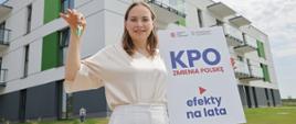 Minister funduszy i polityki regionalnej Katarzyna Pełczyńska-Nałęcz stoi przed budynkiem, w jednej dłoni trzyma dużą kartkę papieru z napisem: KPO zmienia Polskę, efekty na lata, a w drugiej ręce kluczyki