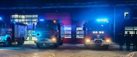 Teren komendy powiatowej psp w brzezinach na placu przed garażami stoją samochody bojowe z włączonymi światłami niebieskimi oraz sygnałami alarmowymi obok stoją strażacy w szeregu na baczność dowódca składa hołd salutując